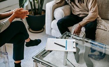 pexels-photo-5699418-5699418 Crop anonymous African American man in casual clothes sitting on sofa and talking to female psychologist during psychotherapy session in modern studio
