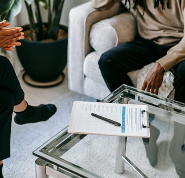 pexels-photo-5699418-5699418 Crop anonymous African American man in casual clothes sitting on sofa and talking to female psychologist during psychotherapy session in modern studio